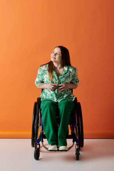 A young woman in vibrant attire sits in a wheelchair against an orange background, looking up with a smile.