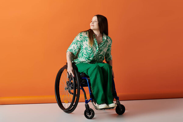 A young woman in vibrant green clothing sits in a wheelchair against a bright orange backdrop.