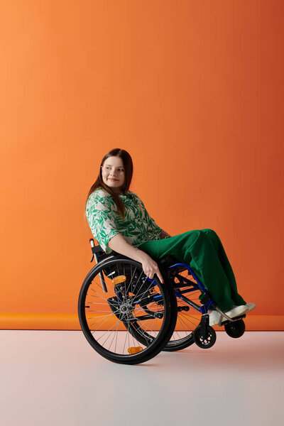 A young woman in vibrant attire sits confidently in a wheelchair against a bright orange background.