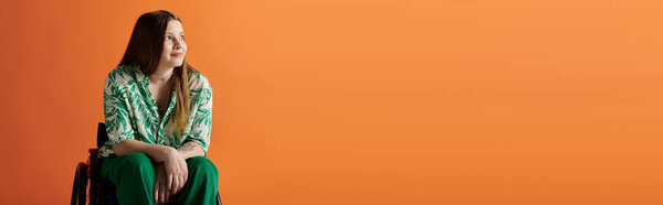 A young woman in a vibrant green and white shirt sits in a wheelchair against a bright orange background.