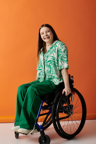 A young woman in vibrant green clothing sits confidently in a wheelchair against a bright orange background.