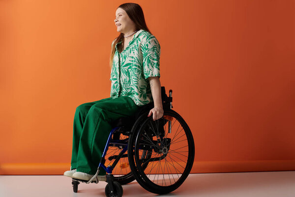 A young woman with bright clothing sits confidently in her wheelchair against an orange backdrop.