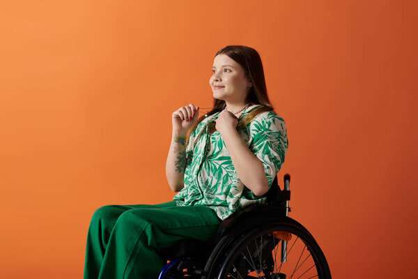 A young woman sits in a wheelchair against an orange background, dressed in vibrant clothing, exuding confidence and joy.