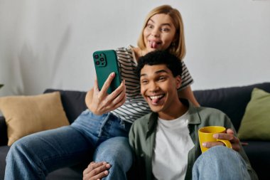 Genç, çok kültürlü bir çift evlerinde bir kanepede oturup aptalca bir selfie çekiyorlar..