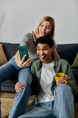 Genç, çok kültürlü bir çift modern dairelerinde komik suratlar yaparken selfie çekiyorlar..