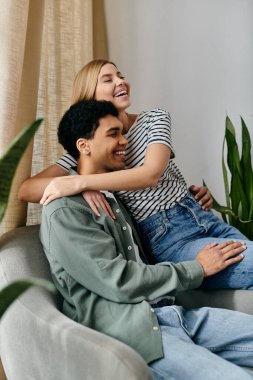 Genç, çok kültürlü bir çift modern bir dairede bir kanepede oturuyor, gülüyorlar ve birbirlerine eşlik ediyorlar..