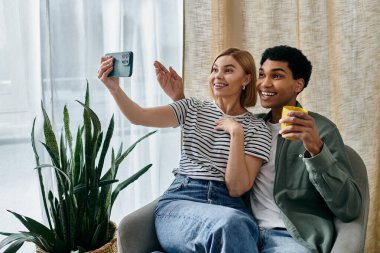 Genç bir ırklar arası çift, modern bir dairede eğlenirken selfie çekmek için gülümsüyor..