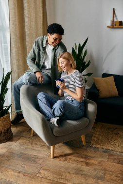 Genç bir çift modern bir dairede birbirleriyle eğleniyor. Kadın gri koltukta oturur ve erkek arkasına yaslanır.