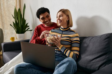 A multicultural couple enjoys a relaxing movie night in their modern apartment. clipart