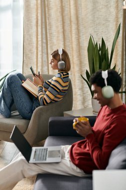 A multicultural couple enjoys a relaxing afternoon in their modern apartment, one reading and the other working on a laptop. clipart