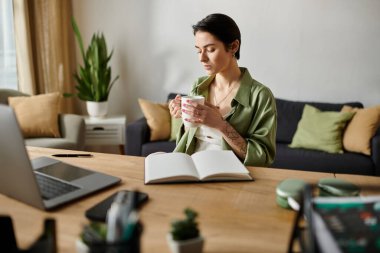 A woman sits at her desk, taking a moment to relax with a cup of coffee while working from home. clipart