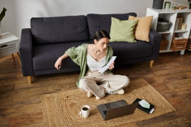 Bir kadın evinde bir halıya oturmuş, dizüstü bilgisayarla çalışıyor..