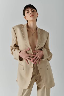 A woman stands in a tan suit, posing confidently in a studio setting. clipart