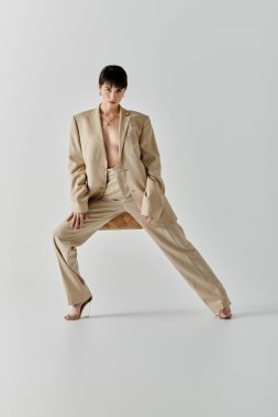 Bej takım elbiseli bir kadın, beyaz bir arkaplana karşı güvenle poz verir..