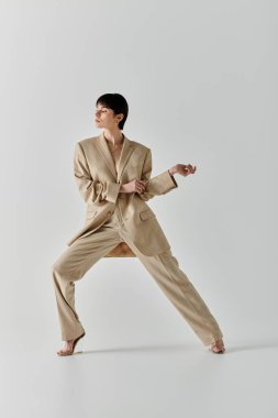 Bej takım elbiseli bir kadın stüdyo odasında bacağı açık poz veriyor..