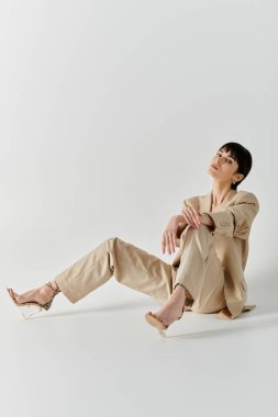 Bir kadın beyaz bir arka planda bronz bir takım elbiseyle poz veriyor..