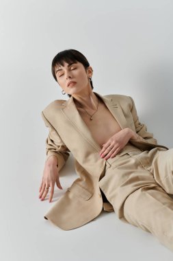 Bej takım elbiseli bir kadın beyaz bir arka fonda yatıyor..