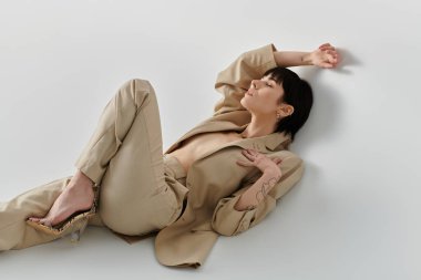 Bej takım elbiseli bir kadın beyaz bir arka planda dinleniyor..