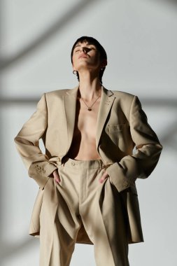 Bej takım elbiseli bir kadın elleri cebinde beyaz bir arka plana karşı poz veriyor..