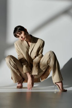 A woman in a tan suit poses in a studio with dappled sunlight. clipart