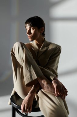 Bir kadın dramatik ışıklandırmayla bej bir takım elbise içinde poz verir..