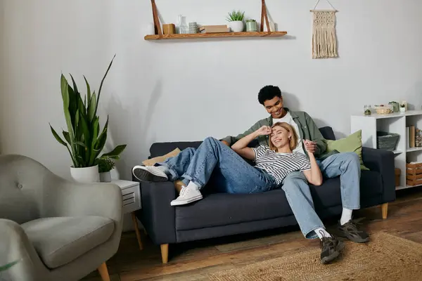 stock image A young multicultural couple laughs and enjoys each others company on a comfortable couch in their modern apartment.