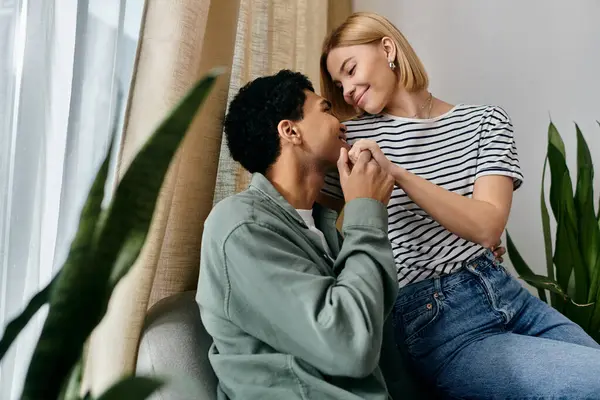 stock image A young multicultural couple shares a tender moment in their modern apartment, with natural light streaming in through the window.