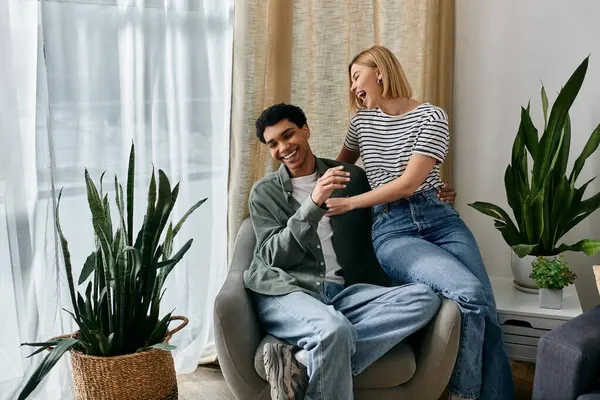 stock image A young multicultural couple shares a laugh in a modern apartment filled with natural light and greenery.