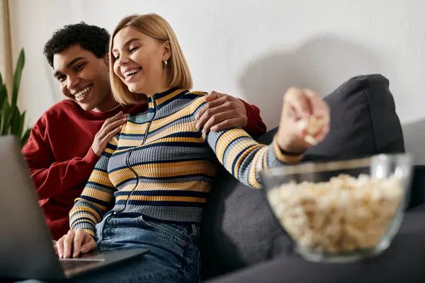 stock image A happy, multicultural couple enjoys a night in, sharing a laugh while watching a movie on a laptop.