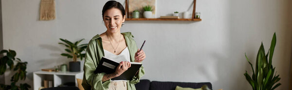 A woman smiles as she takes notes in her home office.