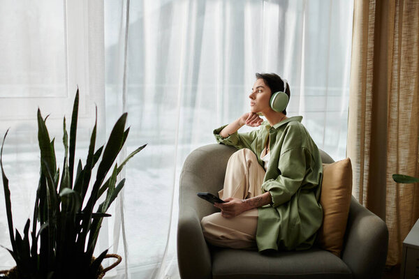 An attractive woman in a green shirt relaxes in her home, wearing headphones.
