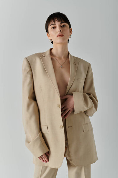 Женщина уверенно позирует в бежевом пиджаке, демонстрируя минималистский стиль.