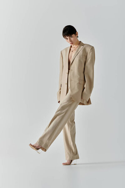 A woman in a beige suit walks forward, her leg extended in a confident pose.