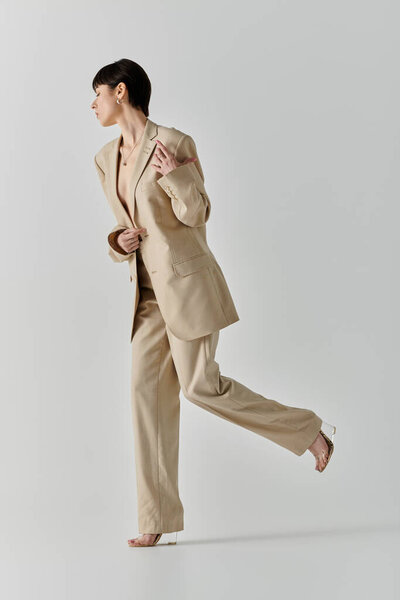 A woman in a beige suit walks confidently with her arms crossed in front of her.