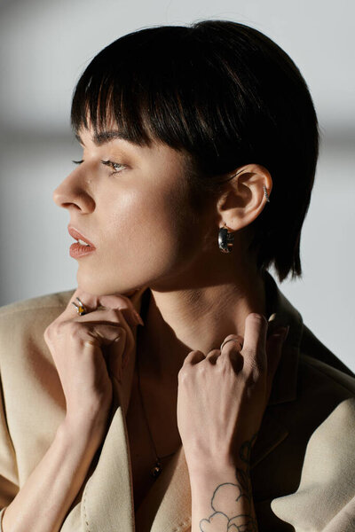 Женщина с черными волосами в бежевой куртке, задумчиво глядя в сторону от камеры.