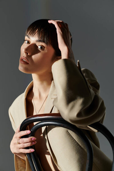 Молодая женщина позирует, опираясь рукой на голову, на фоне мягкого света.