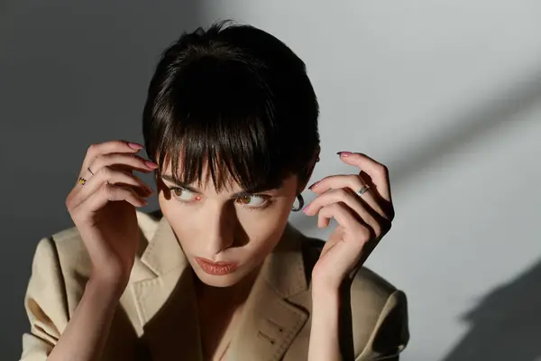 stock image A woman with short, dark hair poses with a thoughtful expression, her hand resting near her face.