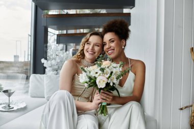A lesbian couple, dressed in white, shares a loving embrace on their wedding day. clipart