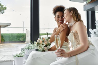 A lesbian couple toasts to their wedding day, smiling and holding a champagne flute. clipart