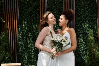 Two brides in white wedding dresses share a loving embrace during their ceremony. clipart