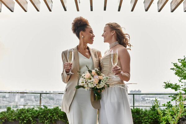 Две невесты тост друг за друга с шампанским на их церемонии свадьбы на крыше.