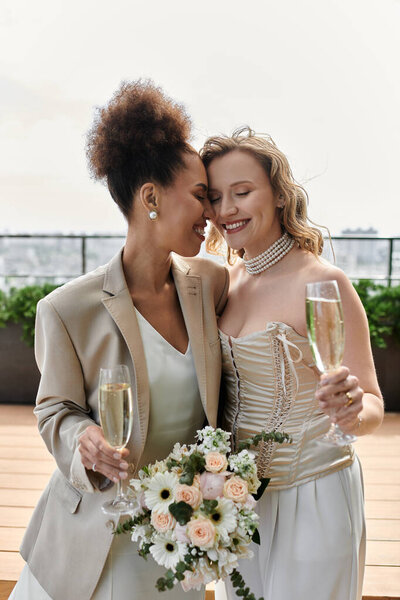 A happy lesbian couple celebrates their wedding with champagne on a rooftop terrace.