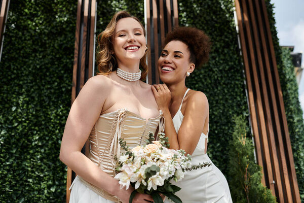 Две невесты стоят вместе, улыбаясь и глядя друг на друга в день их свадьбы.