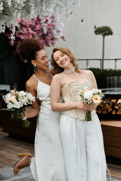 Two brides, dressed in white, embrace and share a happy moment on their wedding day.