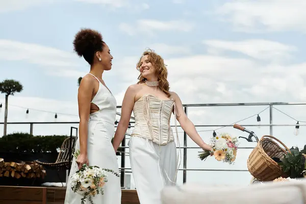 stock image Two brides in white dresses smile with flowers on a rooftop.