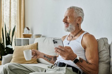 Dövmeli, gri sakallı, olgun bir eşcinsel koltukta dinleniyor ve evinde huzurun tadını çıkarıyor..