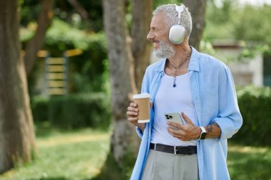 Dövmeli ve gri sakallı olgun bir eşcinsel parkta kahve molası verip kulaklıkla müzik dinliyor..