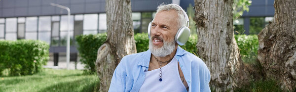 Человек с седой бородой и татуировками слушает музыку в наушниках.