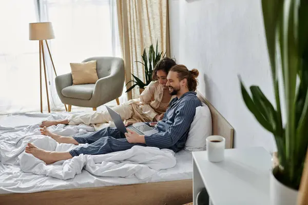 stock image A couple relaxes in bed, sharing a laptop and enjoying a cozy morning together.