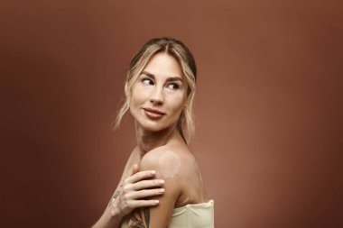 Vitiligo 'su ve dövmesi olan genç bir kadın, omuzları bej bir arka planda çıplak poz veriyor..